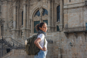 Fototapeta na wymiar A female pilgrim on the Camino de Santiago, carrying a backpack adorned with a scallop shell, finishing her walk in front of the Cathedral of Santiago de Compostela