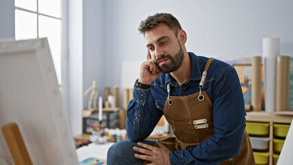Focused young hispanic male artist sitting inside art studio, handsome bearded man engaged in...