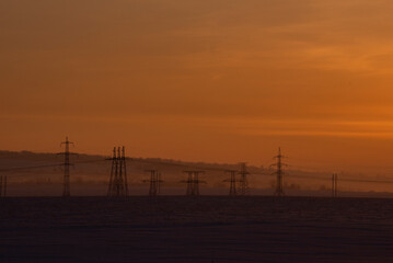 Russia. The South of Western Siberia. High-voltage metal structures against the background of a crimson dawn winter sky.
