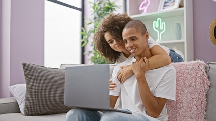 Beautiful couple enjoying a fun, joyful time kissing and working on a laptop while sitting together...