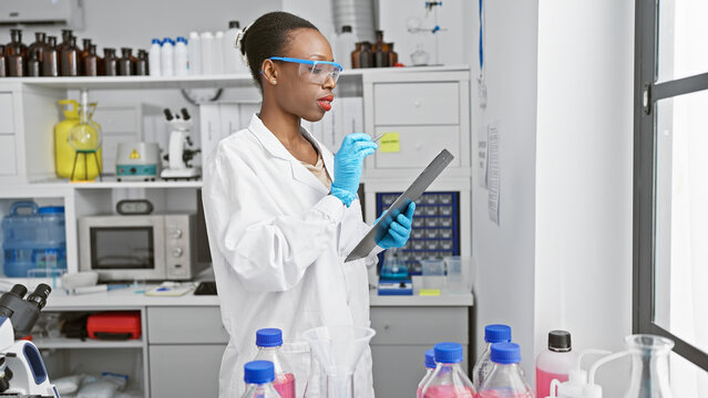 Passionate african american female scientist in lab gloves, fascinated by the power of medical research, deeply engrossed in taking notes at an indoor science laboratory