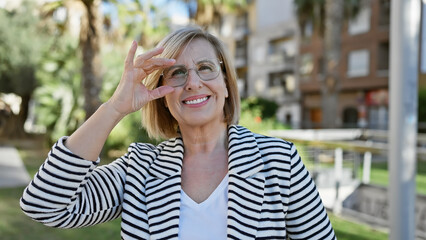 Mature caucasian woman with blonde hair smiling in a striped blazer in a green park