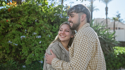 Fototapeta premium A smiling woman and man embrace joyfully in a lush garden, showcasing love and companionship in a natural outdoor setting.