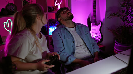 In a neon-lit gaming room, a man and woman relaxedly engage in video games together at night.