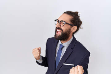 Hispanic man with beard wearing suit and tie very happy and excited doing winner gesture with arms...
