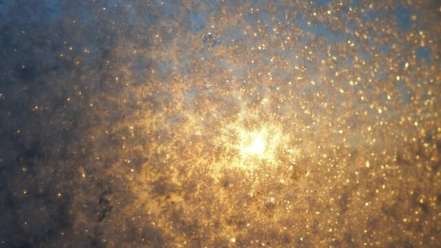 The frosty pattern on window glass occurs due to the condensation of water vapor on glass cooled below 0 degrees. Frost flowers, curls and crystals. Morning yellow-orange low winter sun on the horizon