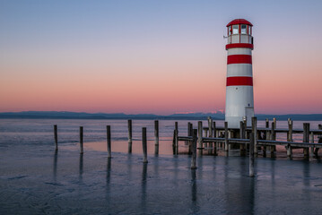 Wooden piles and the frozen Neusiedler See around the striped lighthouse of Podersdorf in...