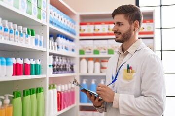Young caucasian man pharmacist smiling confident writing on document at pharmacy