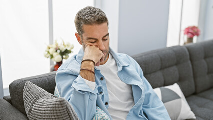 Thoughtful man contemplating while sitting on a gray sofa in a modern living room interior