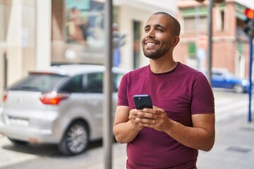 Young latin man smiling confident using smartphone at street