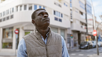 A contemplative african man standing on a city street with buildings and cars in the background