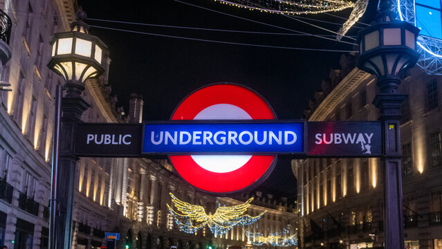 London, UK - December 10 2022 : Illuminated sign of Piccadilly Circus subway station entrance, Bakerloo line. With Christmas lights of regent street in the background at night