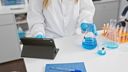 Serious woman scientist working on medical research in lab, hands measuring liquid in test tube, using touchpad on lab table