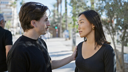 Interracial couple, man and woman, exchanging loving looks on a sunny urban street.