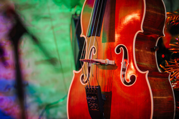 Riga, Latvia - January 18, 2024 - Close-up of a double bass with its curved body, strings, and f-holes, colorful blurred background. - obrazy, fototapety, plakaty