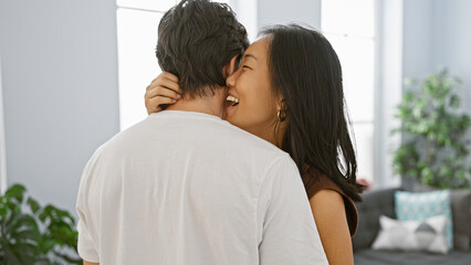 A smiling asian woman embracing a caucasian man in a bright, modern living room, expressing love...