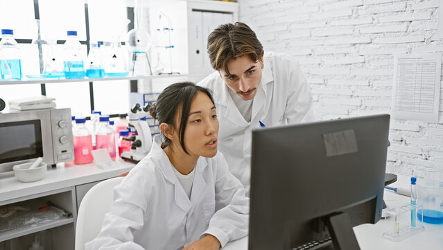 Two scientists, a man and a woman, are analyzing data on a computer in a modern laboratory setting.