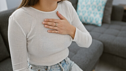 A young hispanic woman in a serene living room, hand on chest, conveying a sense of wellbeing.
