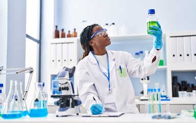 African american woman scientist holding bottle writing on document at laboratory