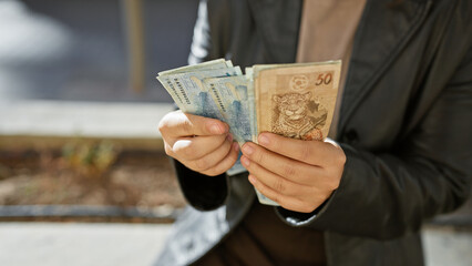 Young hispanic woman holding brazilian currency outdoor in city street.