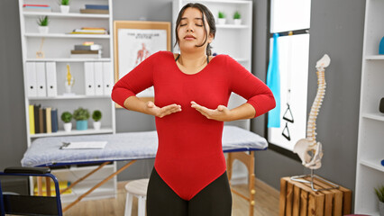 Hispanic woman practicing breathing exercises in a rehab clinic's therapy room, showcasing health and wellness.