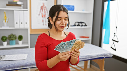 A smiling young woman examines brazilian reais in a bright rehabilitation clinic room.