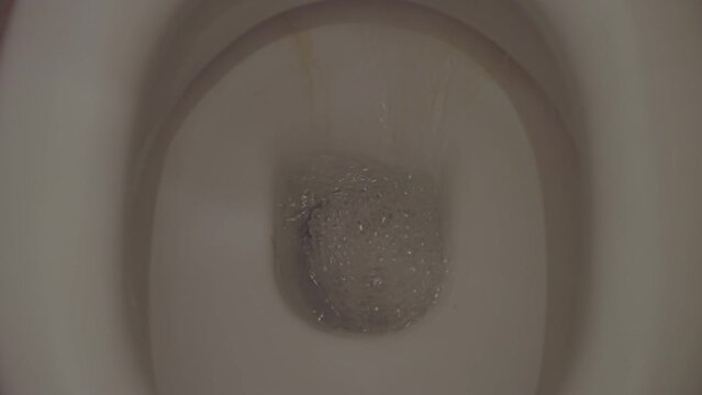 Flushing water in old dirty ceramic toilet bowl, close up view from above. Problem of outdated plumbing in hotels and residential houses