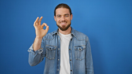 Young hispanic man smiling confident doing ok gesture over isolated blue background