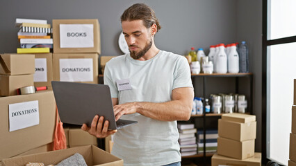 Young hispanic man volunteer using laptop at charity center