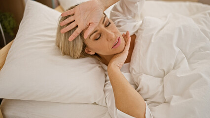 Young blonde woman lying on bed being sick at bedroom