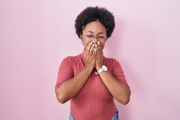 Beautiful african woman with curly hair standing over pink background laughing and embarrassed...