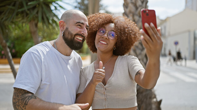 Beautiful couple snapping a fun selfie together on a sunny city street, smartly casual and positively smiling - a vibrant expression of their love and joyful lifestyle.