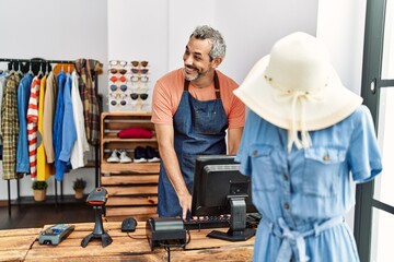 Middle age grey-haired man shop assistant using computer working at clothing store