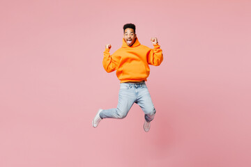 Fototapeta na wymiar Full body exultant young man of African American ethnicity he wearing yellow hoody casual clothes jump high do winner gesture isolated on plain pastel light pink background studio. Lifestyle concept.