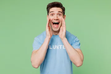 Fotobehang Young man wear blue t-shirt white title volunteer scream about sale discount hands near mouth isolated on plain pastel light green background Voluntary free work assistance help charity grace concept © ViDi Studio