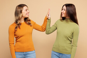 Side view young friends two women they wear orange green shirt casual clothes together meeting together greeting giving high five clapping hands folded isolated on plain pastel light beige background