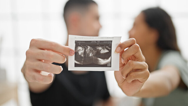 Beautiful couple holding ultrasound baby sitting on bed kissing at bedroom