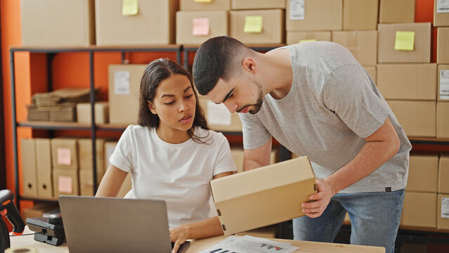 Man and woman working together, two office workers reading package information on laptop in the warehouse