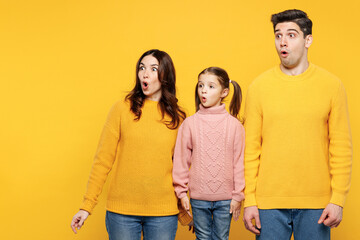 Young shocked scared sad parents mom dad with child kid girl 7-8 years old wear pink knitted sweater casual clothes look aside on area mock up isolated on plain yellow background. Family day concept.