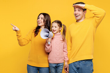 Young fun parents mom dad with child kid girl 7-8 years old wear pink casual clothes hold megaphone scream announces discounts sale point aside isolated on plain yellow background. Family day concept.