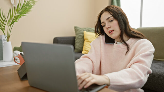 A young woman multitasks using a smartphone and laptop in a cozy home interior, depicting modern remote work.