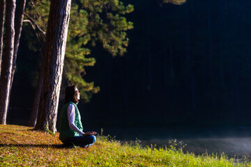 Woman is relaxingly practicing meditation yoga in the forest to attain happiness from inner peace...