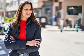 Young beautiful hispanic woman standing with arms crossed gesture at street