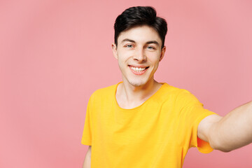 Young smiling cheerful Caucasian man he wear yellow t-shirt casual clothes doing selfie shot pov on mobile cell phone isolated on plain pastel light pink background studio portrait. Lifestyle concept