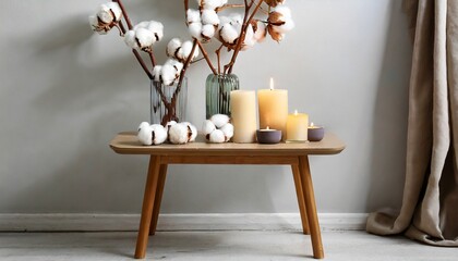 stylish table with cotton flowers and aroma candles near light wall banner for design