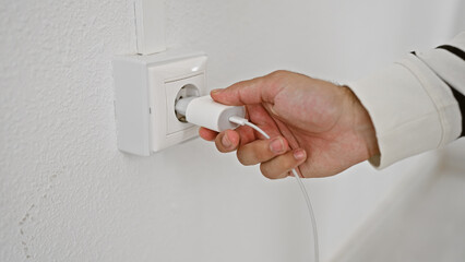 Hispanic man's hands charging energy at home, powering his tech via an electric plug