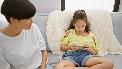 Cozying up at home, mother and daughter engrossed in watching video on smartphone, resting...