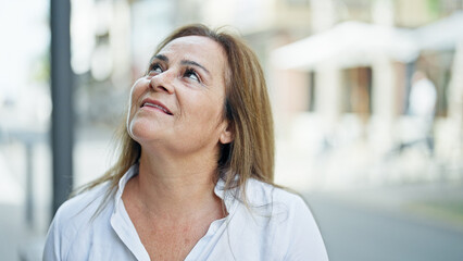 Fototapeta premium Middle age hispanic woman smiling confident looking to the sky at street