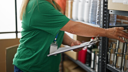 Middle age hispanic woman volunteer writing on checklist at charity center