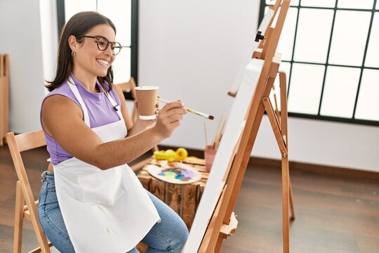 Young beautiful hispanic woman artist drinking coffee drawing at art studio